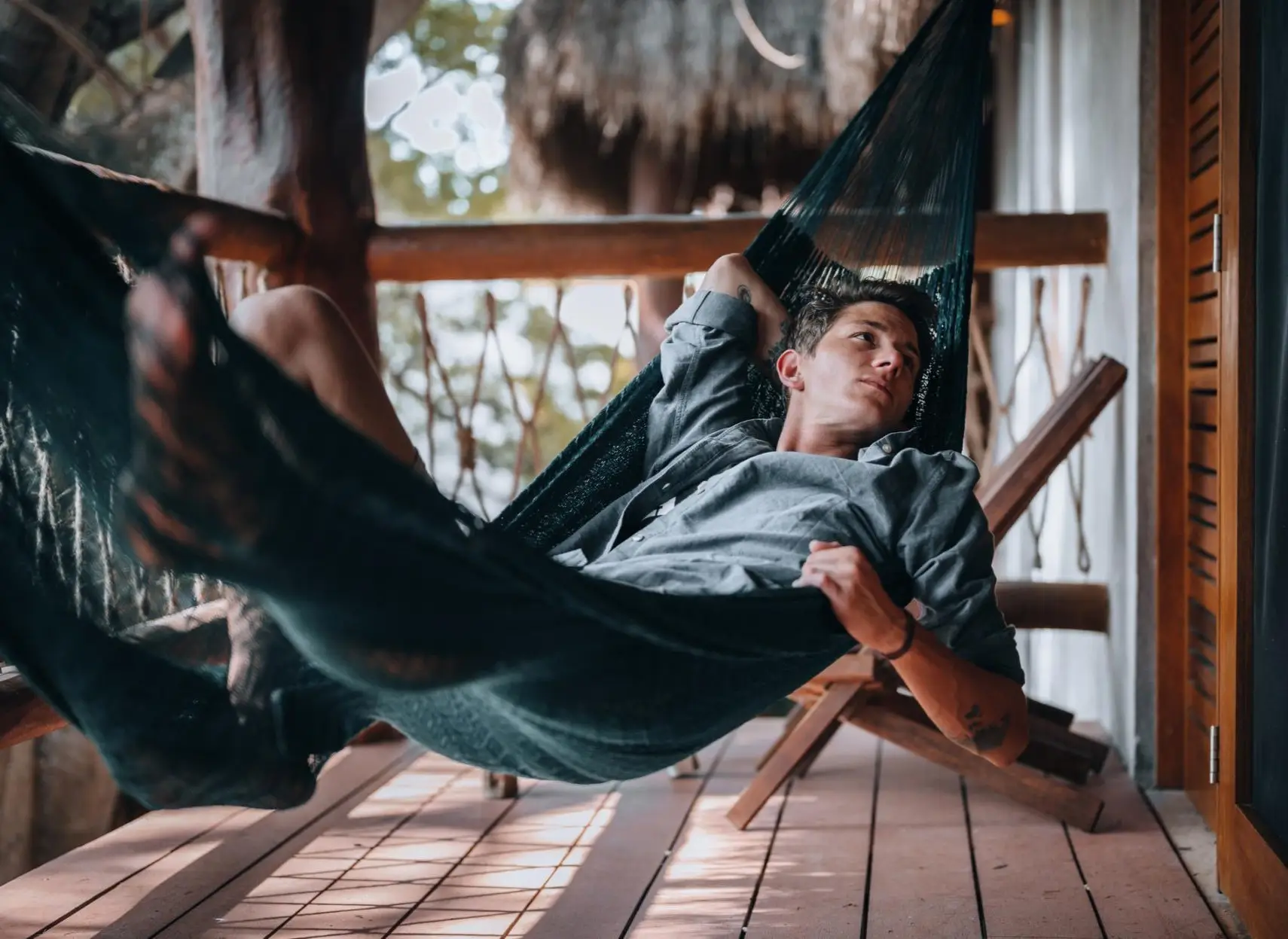 A young urban man relaxing in a hammock hanging on the balcony of a beautiful eco wooden house