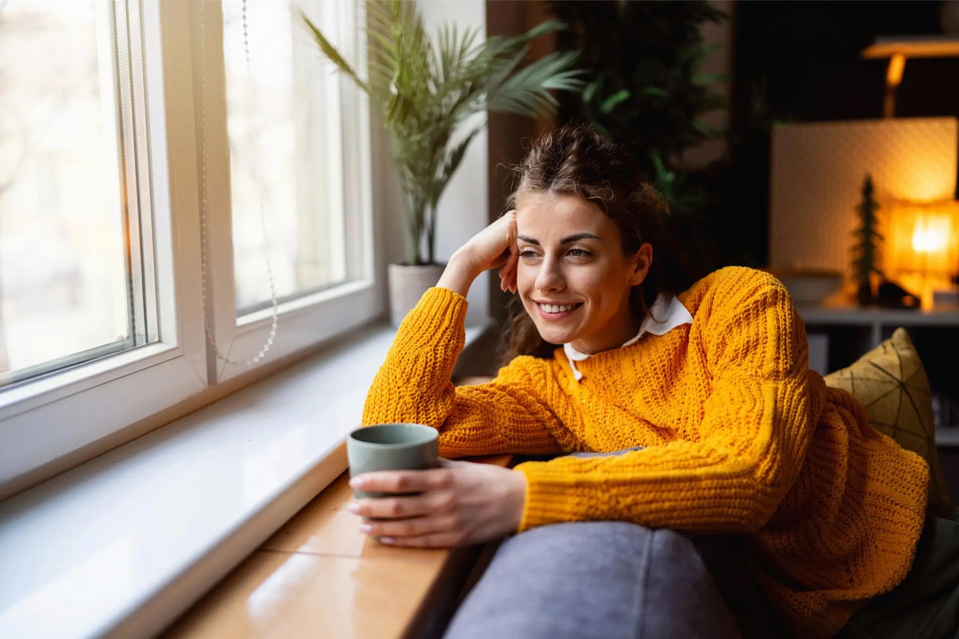 Young Caucasian woman relaxing on the sofa while drinking coffee and looking through window